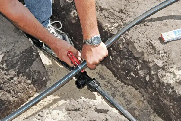 Hände schneiden Kunststoffrohr für die wasserleitung verlegen. Ein T-Stück wird vorbereitet.