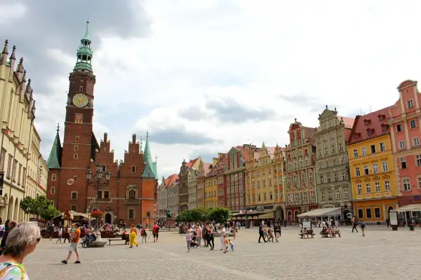 Buntes Treiben auf dem Marktplatz der Breslau Innenstadt. Das Rathaus mit seinem markanten Turm dominiert die Szene, umgeben von farbenfrohen Bürgerhäusern.