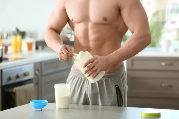 Muskulöser Mann bereitet Proteinshake zu. Informiere dich über mögliche proteinpulver nebenwirkungen, bevor du es verwendest.