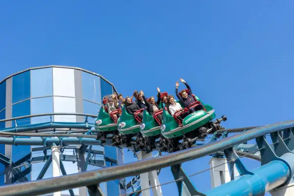 Ludzie na kolejce górskiej wesoło machają rękami. Dzięki **fastpass** uniknęli długiego czekania na tę ekscytującą przejażdżkę.