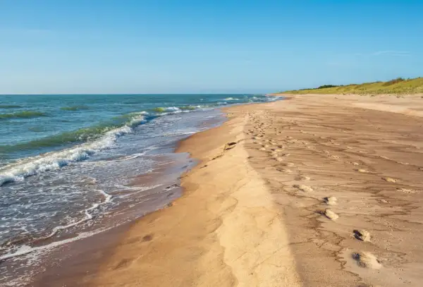 Piękne, dzikie plaże nad Bałtykiem. Fale delikatnie obmywają piaszczysty brzeg, a na piasku widać ślady stóp.