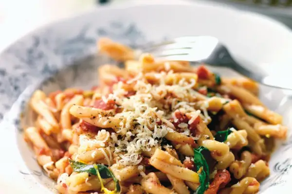 En skål med strozzapreti pasta, toppad med riven ost och en gaffel redo att hugga in.
