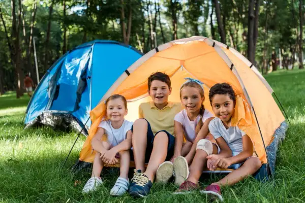 Niños sonríen en una tienda de campaña naranja, disfrutando de una acampada libre en Cantabria.
