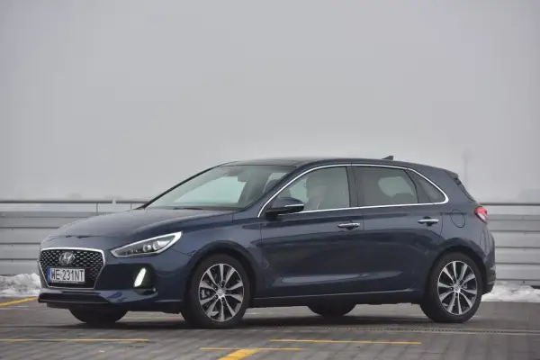 Ciemnoniebieski Hyundai i30 na parkingu. Kierowca w okularach siedzi za kierownicą, gotowy do wymiany żarówki.
