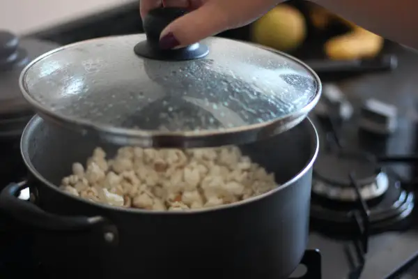 Ręka podnosi pokrywkę garnka, spod której widać gotowy popcorn. Tak właśnie robi się popcorn w garnku!