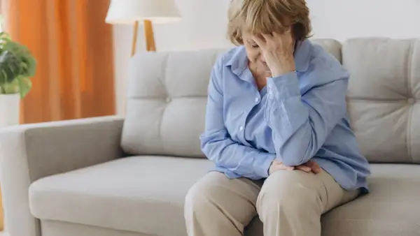Femme âgée assise sur un canapé, la main sur le front, évoquant la recherche d'un hypotension traitement naturel.