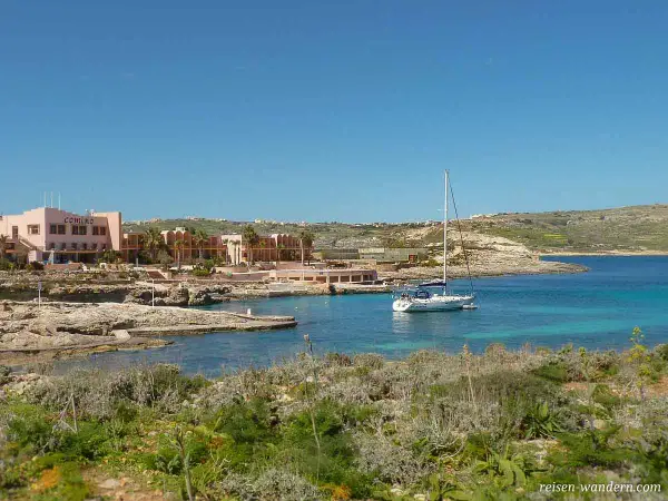 Traumhafter Urlaub auf Malta: Ein Segelboot ankert in einer Bucht vor dem Comino Hotel, umgeben von Felsen und mediterraner Vegetation.