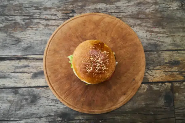 Hamburger z sezamem na drewnianej desce, widok z góry.