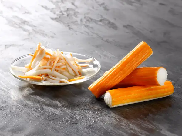Surimi co to? Pomarańczowe paluszki i pokrojone w słupki surimi na talerzyku.