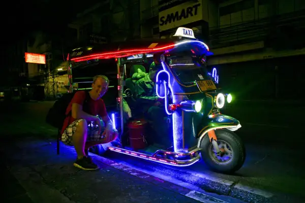 Uśmiechnięty turysta przy neonowym tuk tuk taxi w Tajlandii. Nocne światła tworzą magiczną atmosferę.