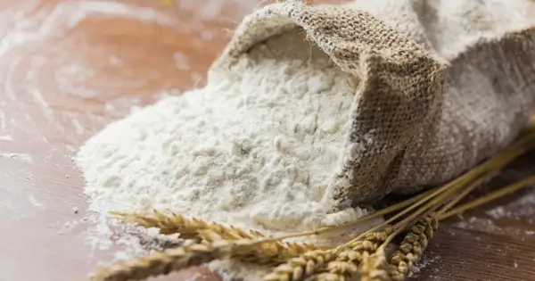 Wsypana z worka mąka pszenna i kłosy zbóż. To właśnie z nich powstaje gluten, kluczowy składnik wypieków.