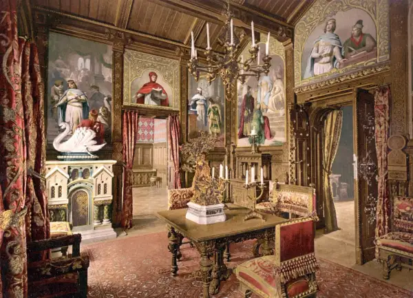 Prunkvoller Salon im Schloss Neuschwanstein innen. Wandmalereien mit Sagenmotiven, ein Kamin mit Schwan, prunkvolle Möbel und ein Kronleuchter schaffen königliches Ambiente.