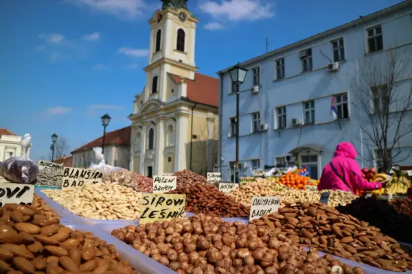 En marknad i Belgrad under en solig helg. Ett överflöd av nötter och torkad frukt säljs framför en kyrka och blå byggnad.