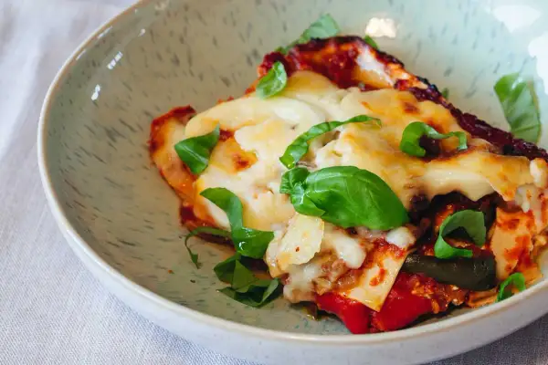 Ein Stück köstliche vegetarische Lasagne mit geschmolzenem Käse und frischem Basilikum in einer Schüssel.