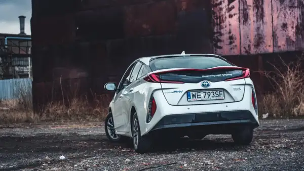 Biały Prius 4 z napędem hybrydowym stoi na tle industrialnego krajobrazu.