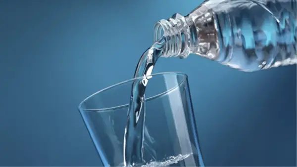 Un filet d'eau pure, riche en magnésium, se verse d'une bouteille dans un verre transparent sur fond bleu.