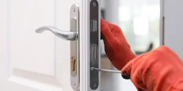 Main tenant utilise un tournevis pour changer la serrure d'une porte blanche.