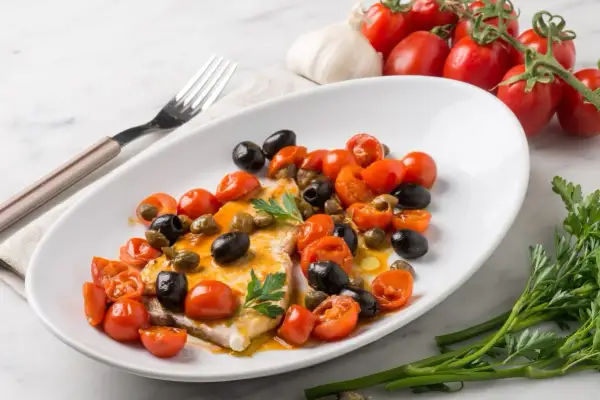 Piatto di pesce spada con pomodorini, olive nere e capperi. Una ricetta mediterranea gustosa e colorata.