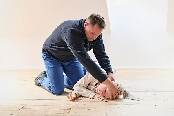 Mann übt die stabile Seitenlage an einer Person auf dem Holzboden.