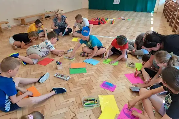 Dzieci w wieku szkolnym biorą udział w zabawach integracyjnych, rysując i kolorując na podłodze.