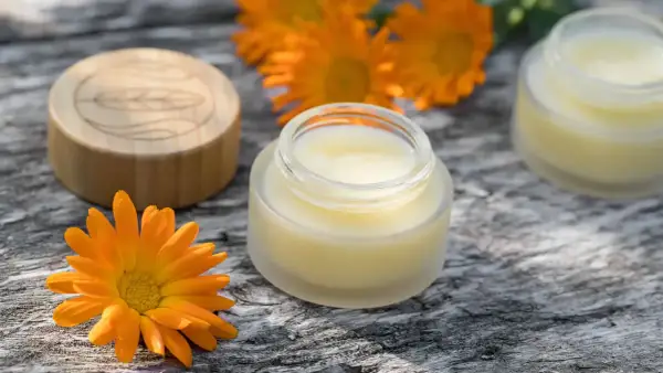 Zutaten für calendula creme selber machen: Ringelblumen, ein Glas mit Creme und ein Holzdeckel.