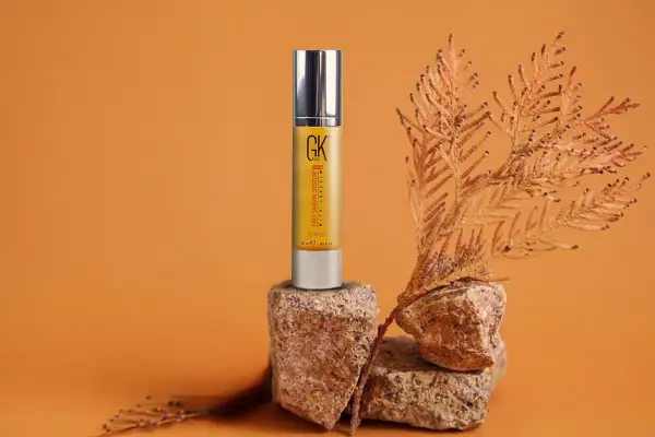 Sérum capilar GK Hair en envase dorado, con ramas secas y rocas. Descubre las maravillosas aceite de argan propiedades para tu cabello.