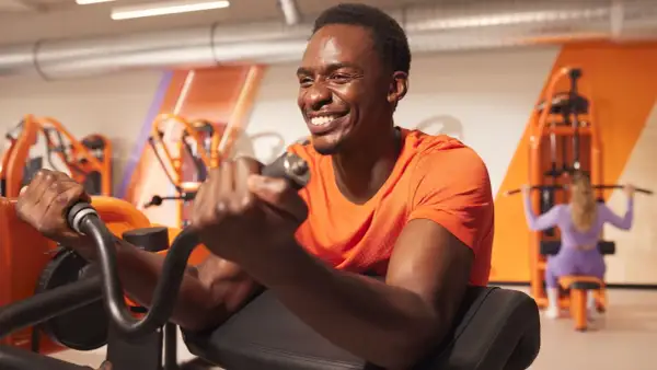 Un homme souriant s'entraîne pour muscler les bras sur une machine de musculation.