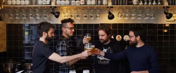 Amici brindano durante una visita birrificio. Bottiglie di birra e bicchieri in primo piano.