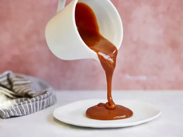 Flüssige Karamellsauce fließt aus einer weißen Kanne auf einen Teller. Ein einfaches karamellsauce rezept für süße Momente.