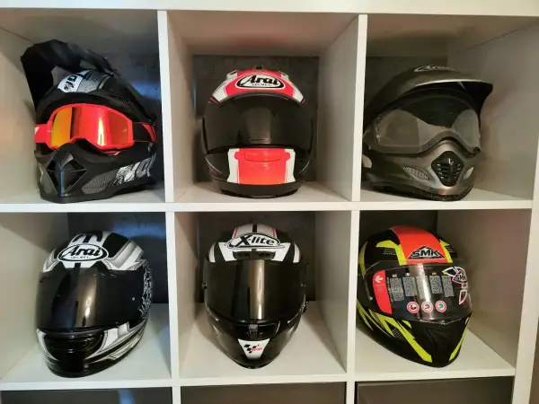 Sześć kasków motocyklowych różnych marek i stylów, ustawionych na półkach.
