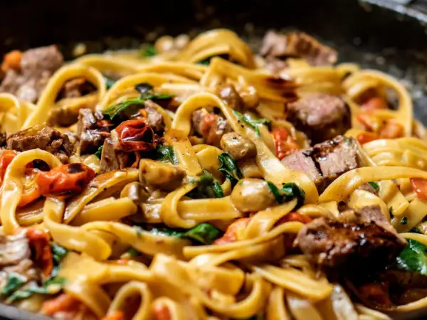 Délicieuses pâtes aux morceaux de bœuf, tomates cerises et champignons. Une idée parfaite pour savoir que faire avec un reste de pâtes !