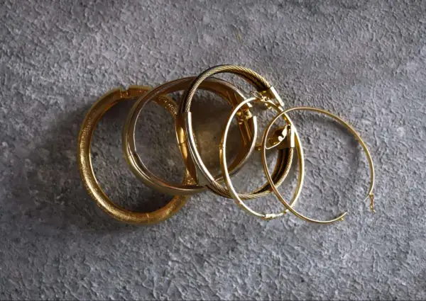 Un grupo de pulseras y aros dorados sobre fondo gris. Aunque el oro no se oxida, estas piezas lucen un brillo que evoca el paso del tiempo.