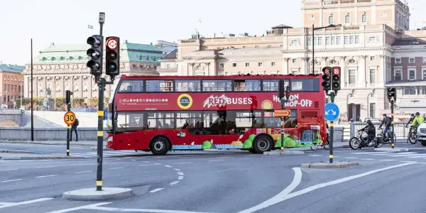 Röd dubbeldäckare för city sightseeing Stockholm passerar en korsning med trafikljus.