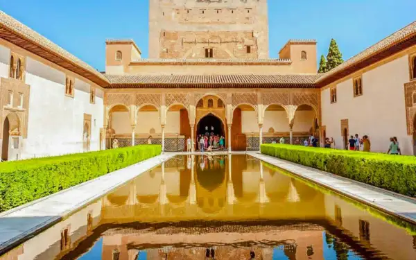 El Patio de los Leones en la Alhambra, con su estanque reflejando la arquitectura y un grupo de visitantes admirando la belleza.