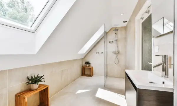 Élégante salle de bain sous comble avec douche moderne, lavabo design et puits de lumière.