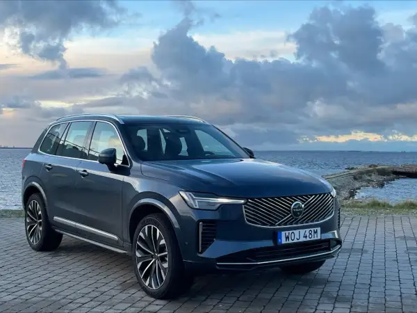 Elegancki, ciemnogranatowy Volvo XC90 2025 zaparkowany nad morzem, z chmurami na niebie.