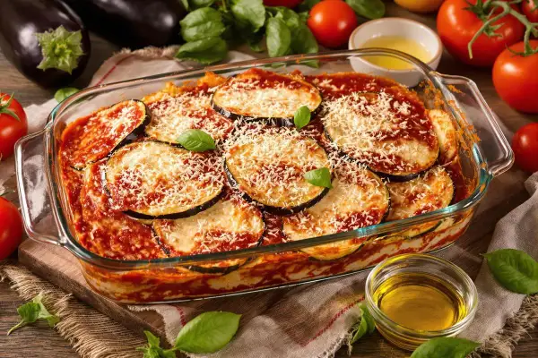 Un plat d'aubergine parmigiana tout juste sorti du four, garni de fromage râpé et de basilic frais.