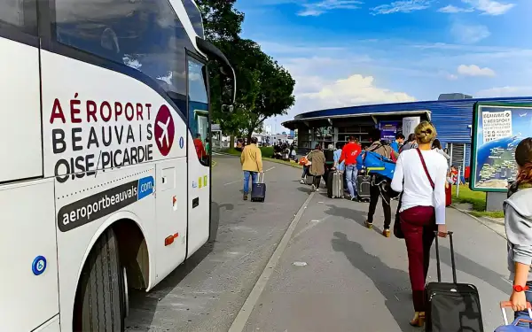 Autobus z napisem "AÉROPORT BEAUVAIS OISE/PICARDIE" czeka na pasażerów z walizkami przed terminalem.
