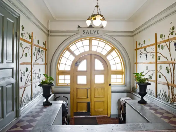 Entréhall med jugendstil hus-känsla. Dubbeldörrar med välvt fönster ovanför. Väggdekorationer med vinrankor.