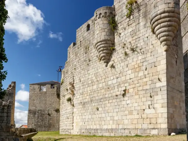 Muros de piedra de un castillo medieval en Castro Caldelas. Un torreón con matacanes y una torre con reloj son parte de lo que ver.