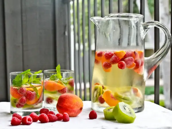 Orzeźwiająca sangria drink z malinami, brzoskwiniami i kiwi w dzbanku i szklankach, ozdobiona miętą.