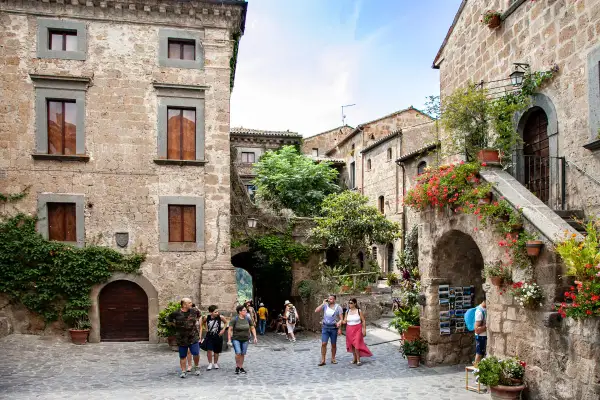 Un vicolo pittoresco nella Tuscia, con case in pietra, fiori colorati e turisti che passeggiano.