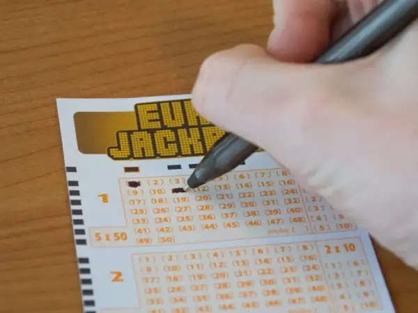 Dłoń z długopisem zaznacza liczby na kuponie Eurojackpot.