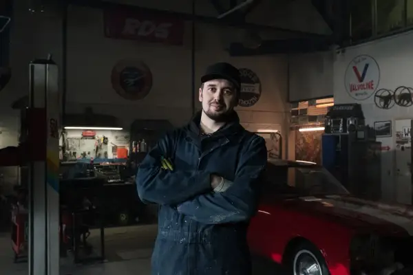 Mechanik w warsztacie z czerwonym autem. Co zrobić, gdy mechanik przetrzymuje auto? Zapytaj o fakturę i termin odbioru.