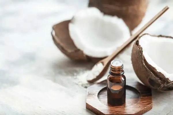 A small bottle of coconut oil sits near a halved coconut and a wooden spoon with coconut flakes. This image prompts the question: is coconut oil safe for cats?