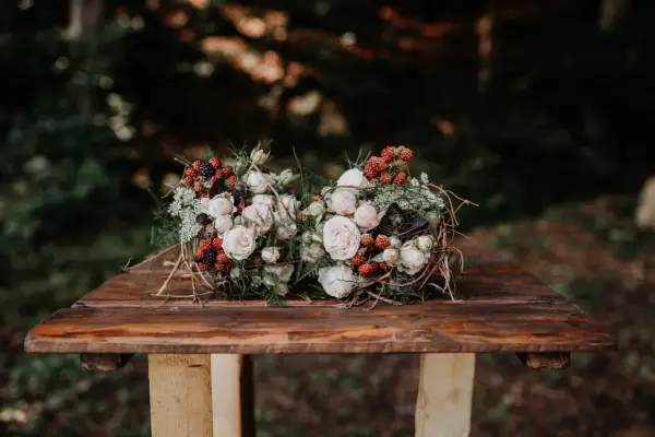 Dwa bukiety ślubne boho z różami, jeżynami i gałązkami na drewnianym stole.
