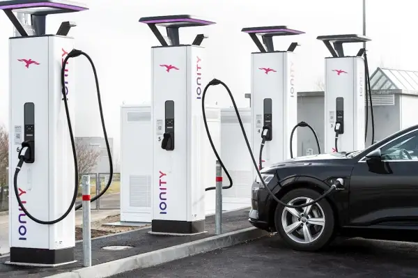 Une voiture électrique noire est branchée à une borne de recharge Ionity. Plusieurs bornes sont alignées, prêtes à alimenter les véhicules.