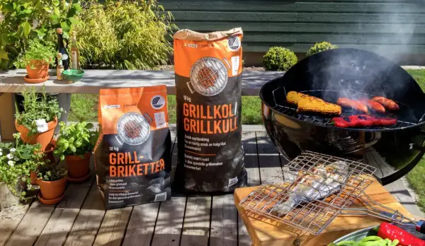 Två säckar med grillkol eller briketter står redo för grillkvällen. Majskolvar, korvar och paprika ryker på grillen.