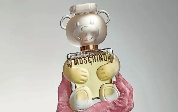 Różowe rękawiczki trzymają uroczy flakon perfum Moschino Toy 2 w kształcie misia.