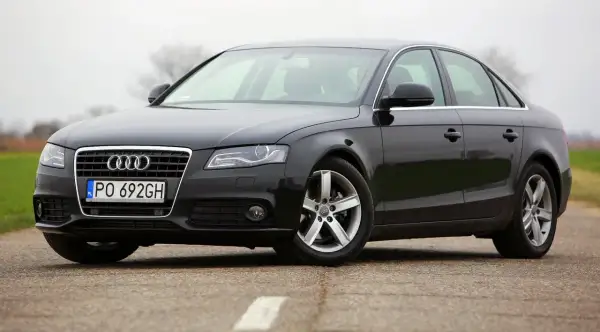 Czarne Audi A4 B8 z polskimi tablicami PO 692GH, z nowymi żarówkami w reflektorach, stoi na drodze.